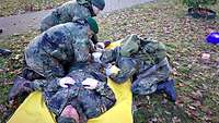 Drei Soldaten knien auf einer Wiese um einen Soldaten herum, der auf einer gelben Plane liegt.