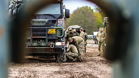 Soldaten ziehen Gleitschutzketten auf einen Lkw-Reifen auf.