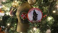 Nahansicht von zwei Patches, die die heilige Barbara zeigen, sowie ein Basecap die am geschmückten Weihnachtsbaum hängen.