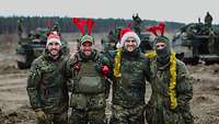 Soldaten stehen vor ihren Panzern und tragen Weihnachtsmützen und Weihnachtsdekoration.