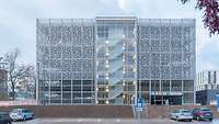 Ein Parkhaus mit Lochblech-Fassade. Davor ein kleiner Parkplatz mit vier Autos.