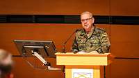 Ein Soldat in Uniform steht an einem Rednerpult mit Wappen Alternativtext