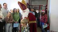 Ein Junge steht vor dem Nikolaus. Im Hintergrund stehen Menschen und freuen sich.