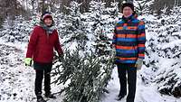 Zwei Gäste stehen mit ihrem Baum und lächeln.
