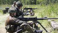 Soldaten im Kampfanzug sitzen an großen Waffen und üben mit diesen. Sie sind in der Natur.