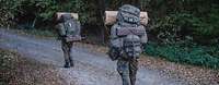 Zwei Soldaten bepackt mit großen Rücksäcken müssen zusätzlich noch einen Baumstamm tragen.