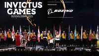 Der Kapitän des deutschens Teams übergibt auf einer Bühne die Fahne an Kanada im Rahmen der Invictus Games.