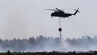 Ein Transporthubschrauber CH-53 verteilt während des Fluges Wasser auf ein Moorbrand Gebiet.