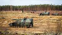 Drei Panzerhaubitzen stehen auf einem Feld auf dem Übungsplatz.
