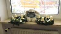 Plüschhase sitzt bei zwei Adventskränzen