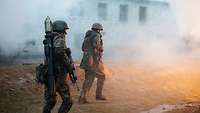 Zwei Soldaten gehen an einem Gebäude entlang. Sie sind in Nebel eingehüllt.