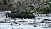 Ein getarnter Kampfpanzer steht auf der winterlich verschneiten Schießbahn.