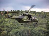 NH-90 - Hubschrauber des Deutschen Heeres Ein Militärhubschrauber fliegt über einen Wald. Ein Soldat schaut dabei aus der geöffneten Tür.