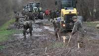 Deichbau Winterhochwasser 2024 Soldatinnen uns Soldaten mit Schaufel stehen an einem Deich. Viel Traktoren sind zu sehen