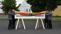 Mehrere Personen ziehen eine Deutschlandflagge von einem Schild, auf dem ein Name steht