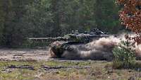 Ein Panzer fährt durch einen Wald und wirbel dabei Staub in die Luft.