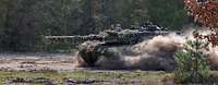 Ein Panzer fährt durch einen Wald und wirbel dabei Staub in die Luft.