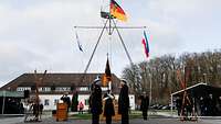 Sechs Personen in Marineuniform stehen sich vor einer Truppenfahne gegenüber.