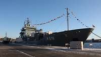 Ein gvraues Schiff ist in einem Hafen an der Pier