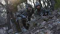 Zwei Soldaten befinden sich in einer Stellung im Wald.