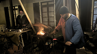 Ein Schmied hält ein Eisen in das Feuer und das Eisen glüht.