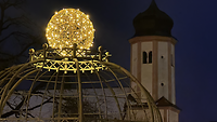 Beleuchtete Kugel vor einem Kirchturm.