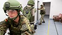Drei Soldaten in einem Hausflur. Die Militärpolizistin sichert zwei Militärpolizisten, die in einen Raum eindringen wollen.