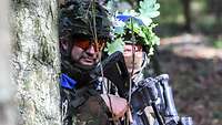 Zwei getarnte Soldaten im Wald hinter Bäumen. 