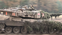 Ein Soldat blickt während der schnellen Fahrt im Gelände aus der Luke eines getarnten Panzers.