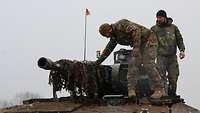Ein deutscher und ein slowenischer Soldat stehen auf einen Schützenpanzer.