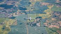 Feldlandschaft aus der Vogelperspektive mit neun Flugzeugen in Formation. 