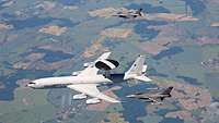 Eine Boeing E-3A AWACS und zwei US-amerikanische Kampfjets F-16 fliegen gemeinsam in Formation.