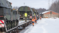 Mehrere Gefechtsfahrzeuge stehen auf Bahnwaggons.