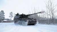Ein gepanzerten Kettenfahrzeug wirbelt den Schnee auf den verschneiten Straßen Litauens auf.