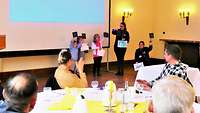 Kinder zeigen den Gästen im Saal ihre selbst gebastelten und gemalten Bilder.