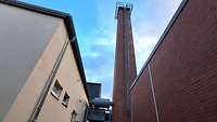 Zwei Industriebauten von außen, zwischen ihnen ragt ein Schornstein in die Höhe