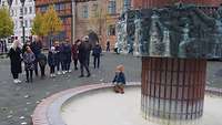 Eine Menschgruppe steht vor einem dekorativem Brunnen in Schwerin.