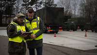 Zwei Personen stehen vor einem Bundeswehr-Fuhrpark und blicken auf ein Tablet, auf dem die Software YARDED läuft. 