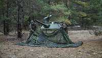 Zwei Soldaten bauen eine Panzerturm-Attrappe in einem Waldstück auf