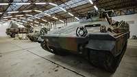 Attrappen von Militärfahrzeugen stehen in einer Halle. Im Vordergrund ein Schützenpanzer Marder.