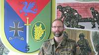 Ein Soldat blickt in die Kamera, im Hintergrund ein Kompaniewappen.