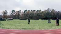 Ein Soldat steht auf einem Platz vor vielen angetretenen Soldaten.