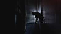 230525_FBER_PHT366.jpg Eine Silhouette einer Person befindet sich in einem dunklen Raum und wird durch ein Licht leicht angestrahlt.