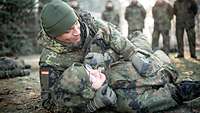 Zwei Soldaten die auf dem Boden liegen, im Hintergrund stehen weitere Soldaten.