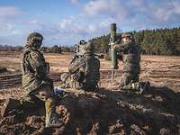 Auf einem Feld knien drei Soldaten neben einer Panzerabwehrwaffe mit einem Lenkflugkörper.