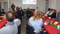 Mehrere Menschen sitzen in einem Saal und hören einen Vortrag.