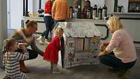 Kinder spielen mit einem Papphaus.