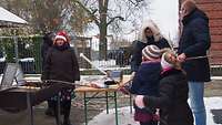 Drei Kinder stehen vor einem Grill und machen Stockbrot.