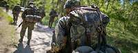 Mehrere Soldaten marschieren mit ihrer Ausrüstung im Gelände.