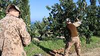 Auf der Baufläche steht ein Soldat mit einer Spitzhacke und benutzt sie. Ein anderer Soldat notiert sich etwas.